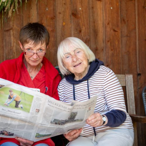 Pflegekraft und Seniorin lesen zusammen eine Zeitung aus Mecklenburg Vorpommern