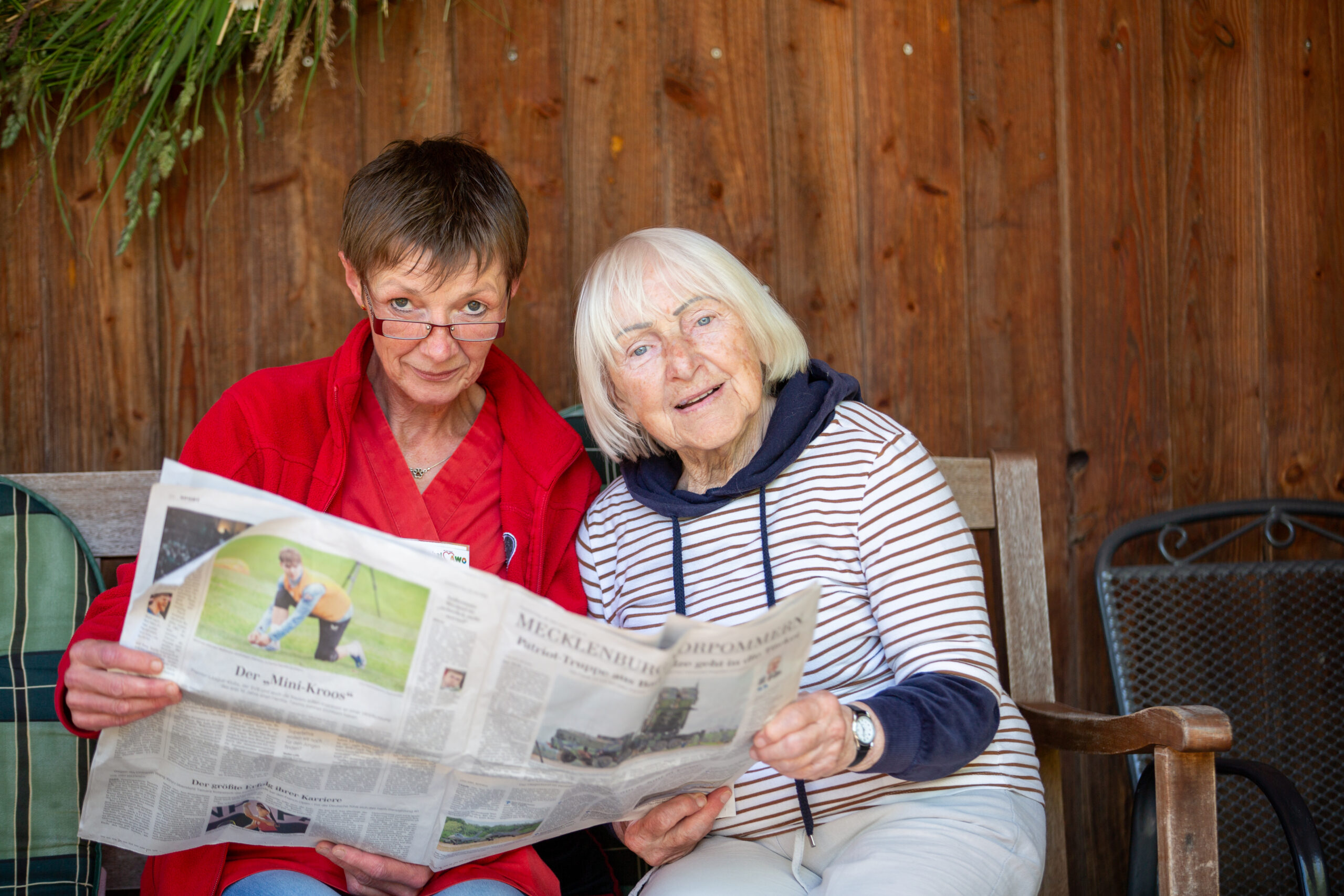 Pflegekraft und Seniorin lesen zusammen eine Zeitung aus Mecklenburg Vorpommern